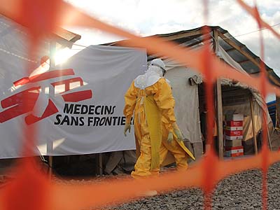 Person in protective clothing walks by a Medecins Sans Frontiers banner